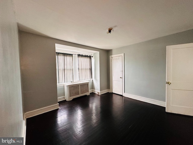 unfurnished room featuring dark hardwood / wood-style floors and radiator heating unit