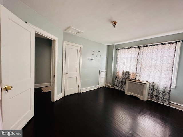 unfurnished bedroom with dark wood-type flooring and radiator heating unit