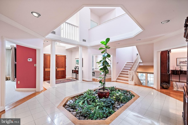 foyer entrance featuring crown molding, tile flooring, a towering ceiling, and ornate columns