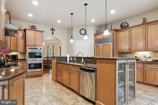 kitchen featuring stainless steel appliances, a kitchen island with sink, decorative light fixtures, backsplash, and sink