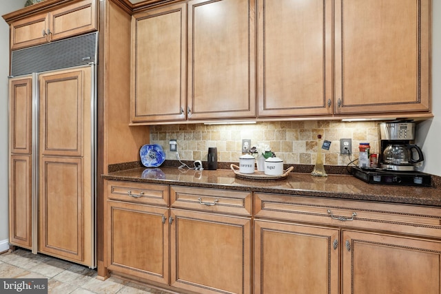 kitchen featuring paneled fridge, dark stone countertops, tasteful backsplash, and light tile floors