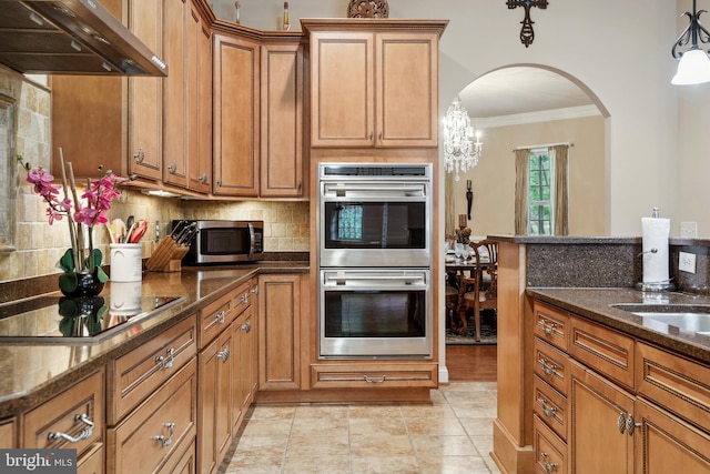 kitchen with crown molding, stainless steel appliances, dark stone counters, wall chimney exhaust hood, and tasteful backsplash