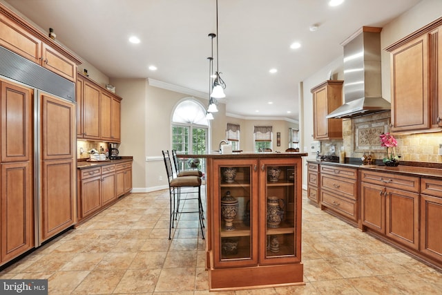 kitchen featuring tasteful backsplash, light tile floors, wall chimney exhaust hood, a kitchen bar, and paneled built in fridge