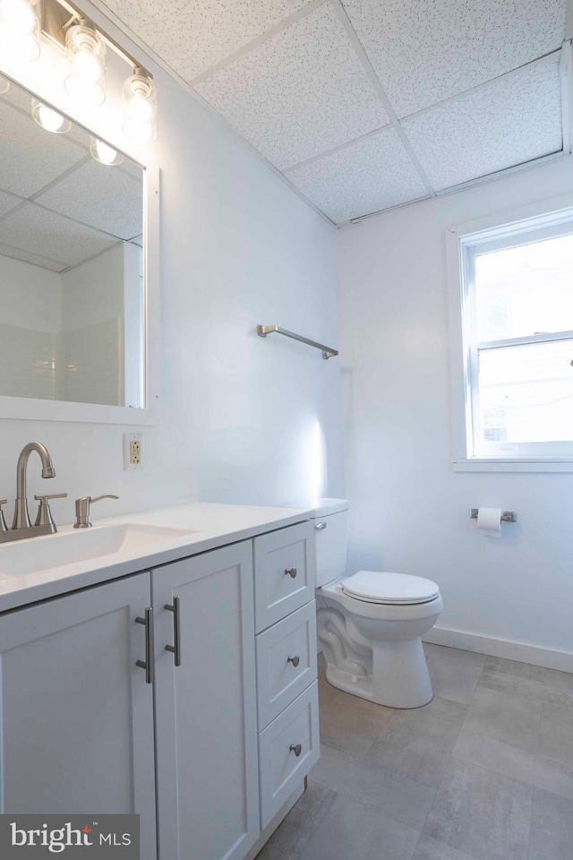 bathroom with vanity with extensive cabinet space, toilet, tile floors, and a drop ceiling