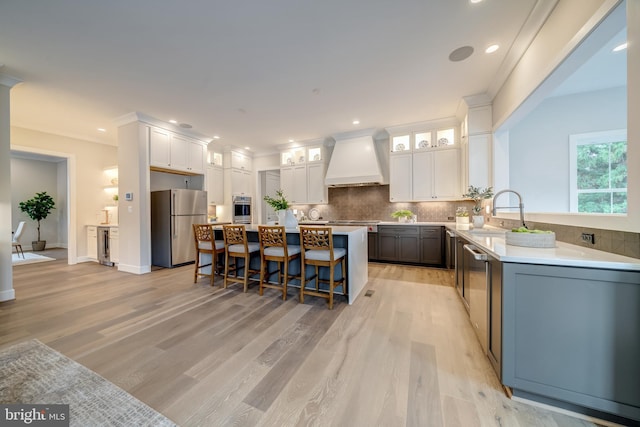 kitchen with appliances with stainless steel finishes, white cabinets, light hardwood / wood-style flooring, and custom exhaust hood