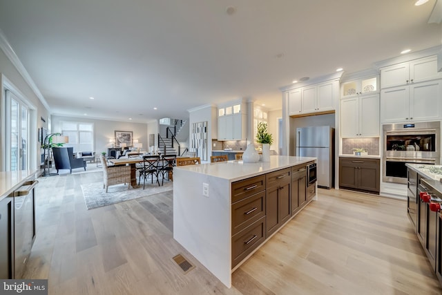 kitchen featuring light hardwood / wood-style flooring, a kitchen island, stainless steel appliances, backsplash, and white cabinetry