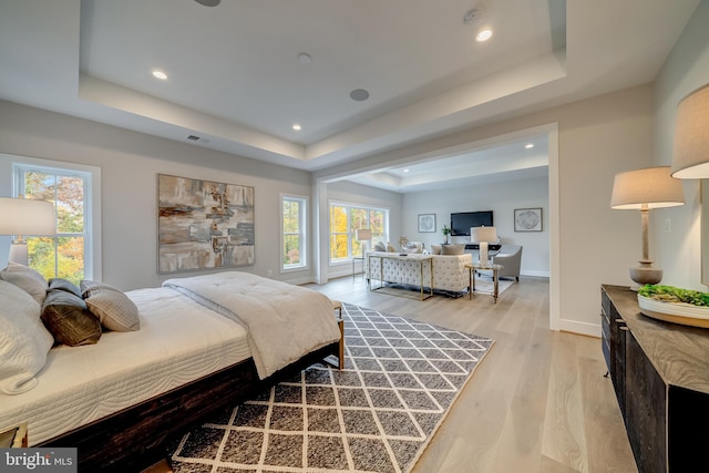 bedroom featuring a raised ceiling, light hardwood / wood-style floors, and multiple windows