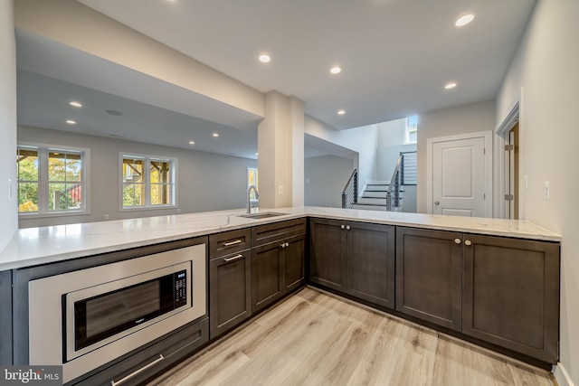 kitchen featuring light hardwood / wood-style floors, light stone countertops, dark brown cabinets, and stainless steel microwave