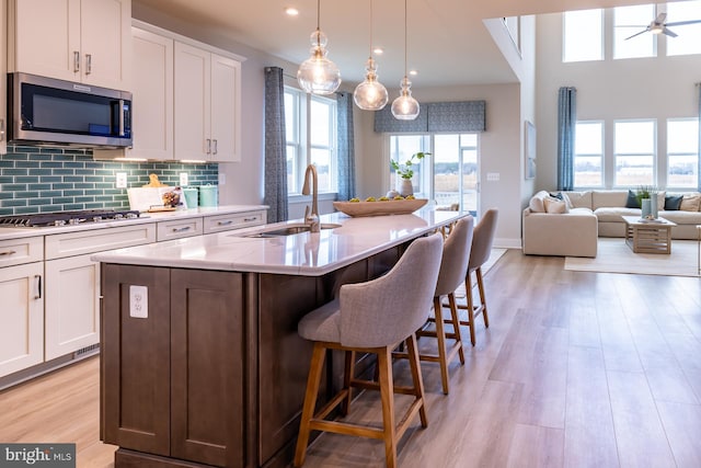 kitchen featuring tasteful backsplash, stainless steel appliances, a center island with sink, light wood-type flooring, and white cabinetry