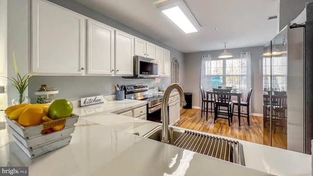 kitchen with appliances with stainless steel finishes, light wood-type flooring, white cabinetry, and pendant lighting