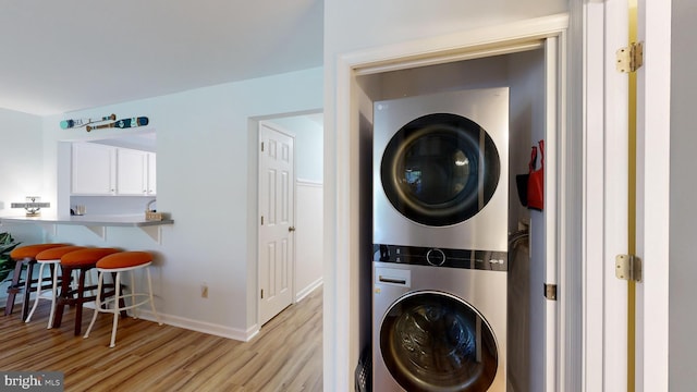 clothes washing area with light hardwood / wood-style floors and stacked washer and clothes dryer