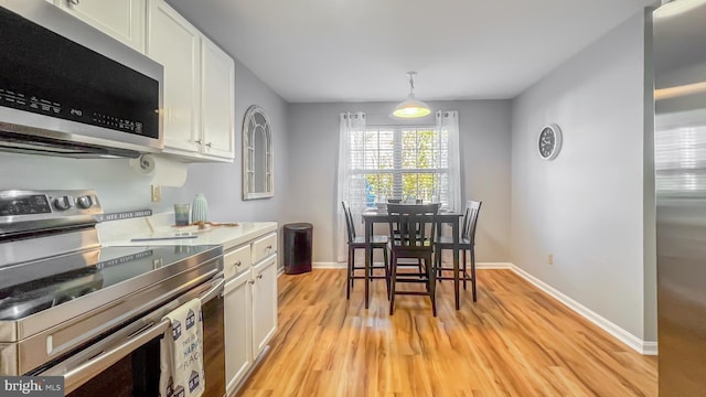 kitchen with white cabinets, decorative light fixtures, stainless steel appliances, and light hardwood / wood-style flooring