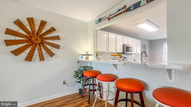 kitchen with white cabinets, a kitchen breakfast bar, kitchen peninsula, and hardwood / wood-style floors