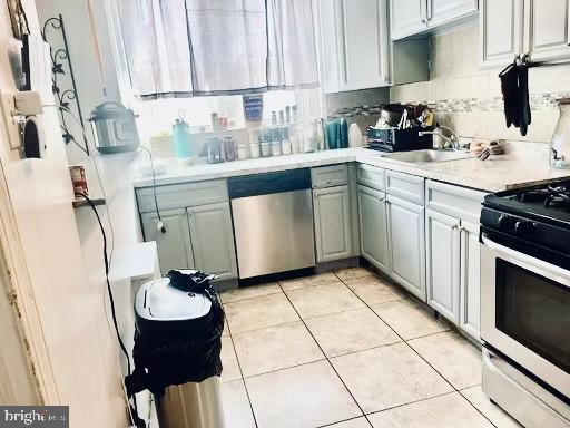 kitchen with stainless steel dishwasher, range with gas stovetop, sink, tasteful backsplash, and light tile floors