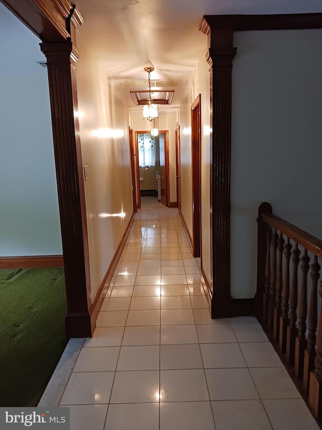 corridor featuring light tile patterned floors, ornate columns, a notable chandelier, and crown molding