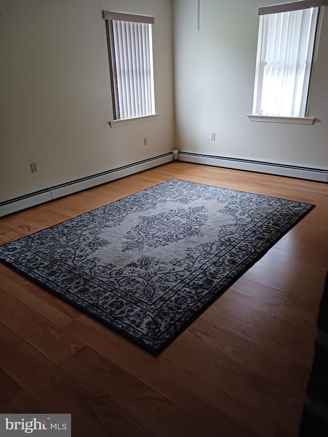 unfurnished room with hardwood / wood-style floors and a baseboard heating unit