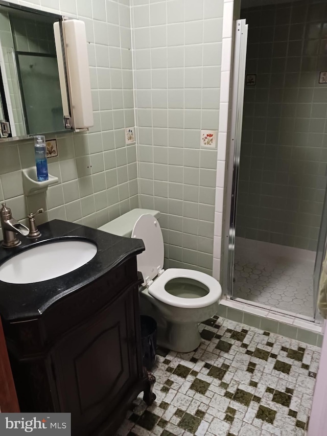 bathroom featuring walk in shower, tile patterned flooring, toilet, vanity, and tile walls