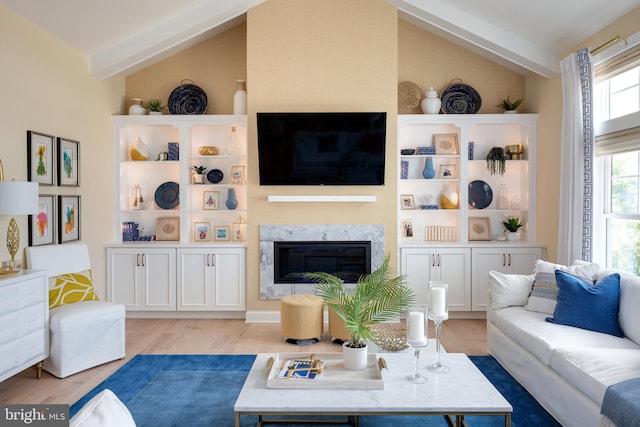 living room with a high end fireplace, lofted ceiling with beams, and light hardwood / wood-style floors