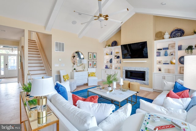 living room with ceiling fan, built in shelves, vaulted ceiling with beams, and light hardwood / wood-style flooring