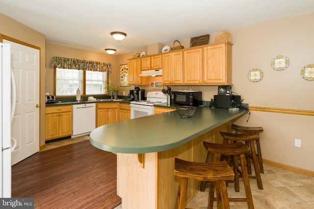 kitchen with tile flooring, white appliances, kitchen peninsula, sink, and a kitchen bar