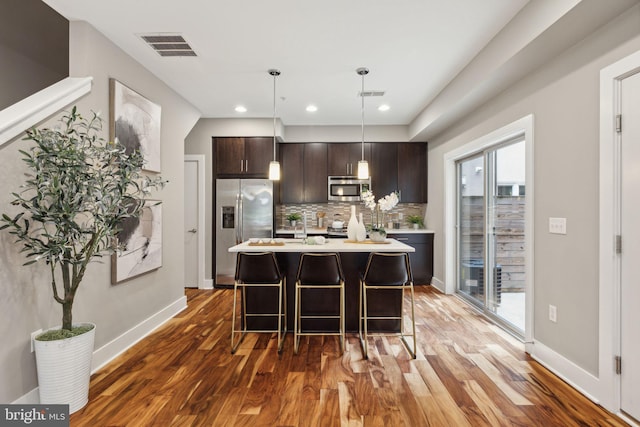 kitchen featuring dark brown cabinetry, a kitchen island with sink, a healthy amount of sunlight, and appliances with stainless steel finishes