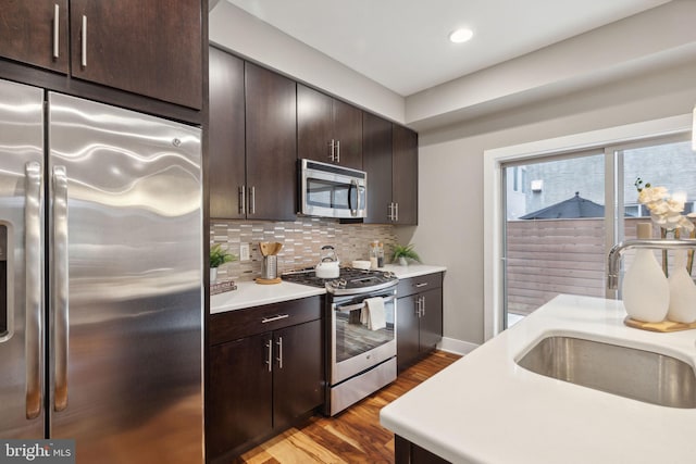 kitchen with sink, tasteful backsplash, dark brown cabinets, light hardwood / wood-style floors, and stainless steel appliances