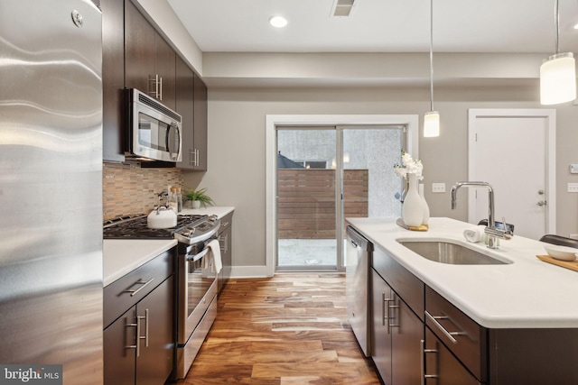 kitchen featuring sink, hanging light fixtures, light hardwood / wood-style floors, dark brown cabinets, and appliances with stainless steel finishes