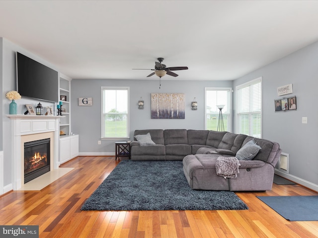 living room featuring built in shelves, ceiling fan, and light hardwood / wood-style flooring