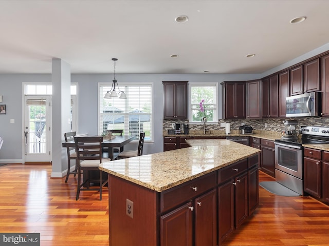 kitchen featuring light hardwood / wood-style floors, a kitchen island, tasteful backsplash, appliances with stainless steel finishes, and pendant lighting