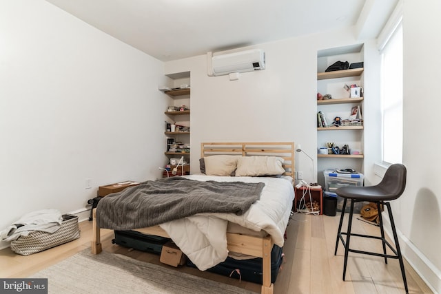 bedroom with a wall mounted AC and light hardwood / wood-style flooring