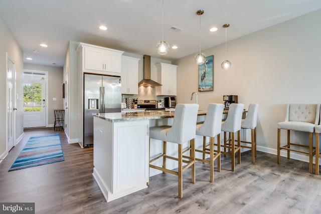 kitchen with light hardwood / wood-style floors, stainless steel appliances, hanging light fixtures, light stone countertops, and wall chimney exhaust hood