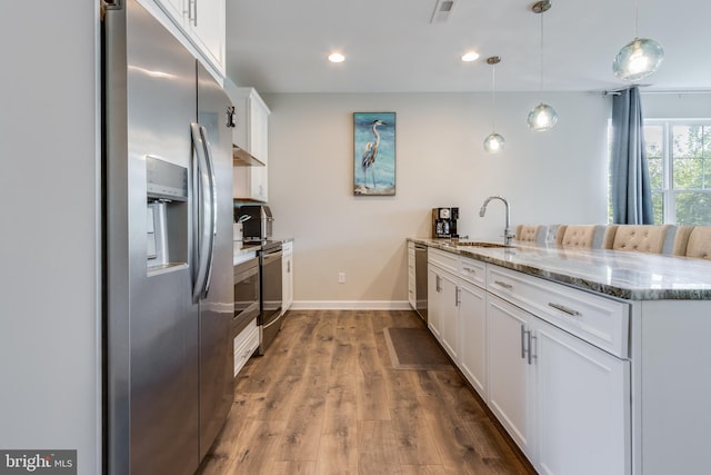 kitchen featuring wood-type flooring, light stone counters, hanging light fixtures, sink, and white cabinets