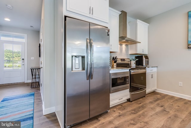 kitchen with hardwood / wood-style floors, tasteful backsplash, stainless steel appliances, wall chimney range hood, and white cabinetry