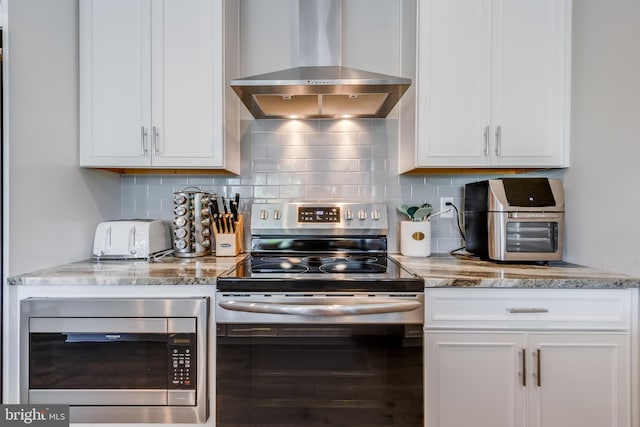 kitchen featuring wall chimney range hood, stainless steel appliances, and white cabinets