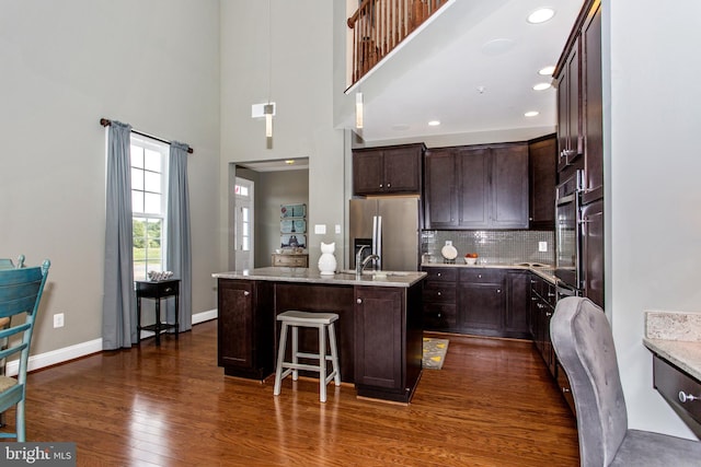 kitchen featuring tasteful backsplash, stainless steel appliances, a center island with sink, dark wood-type flooring, and hanging light fixtures