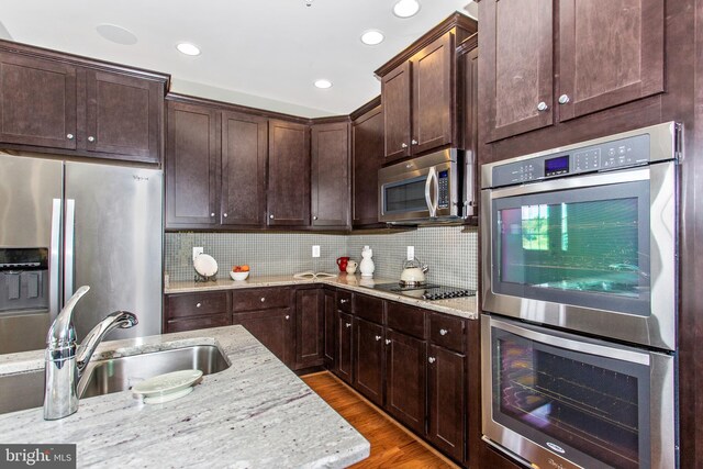 kitchen with light stone counters, stainless steel appliances, backsplash, hardwood / wood-style flooring, and sink