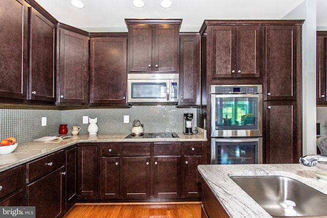 kitchen with appliances with stainless steel finishes, light hardwood / wood-style floors, tasteful backsplash, and light stone counters