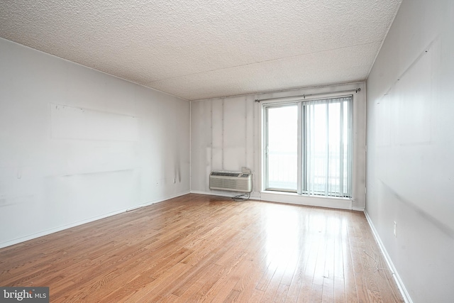 spare room featuring light hardwood / wood-style flooring, a textured ceiling, and a wall mounted air conditioner