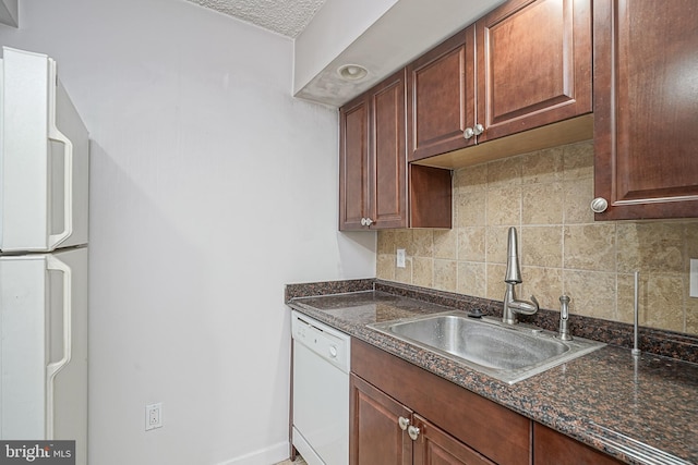 kitchen featuring tasteful backsplash, dark stone countertops, sink, white appliances, and a textured ceiling