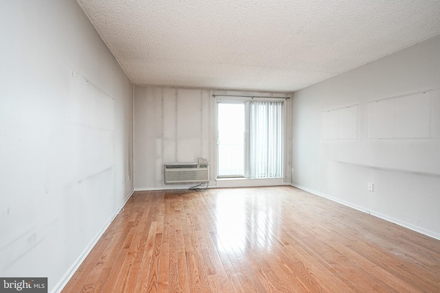 spare room featuring a wall mounted AC, light hardwood / wood-style flooring, and a textured ceiling