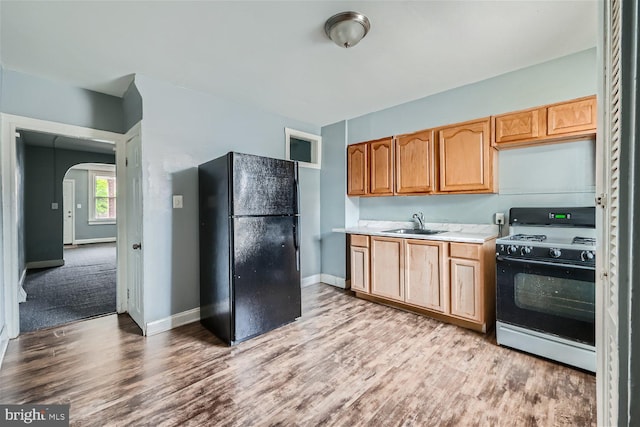 kitchen with black fridge, hardwood / wood-style floors, white gas range oven, and sink