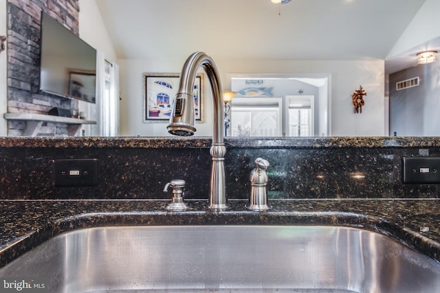 interior details featuring sink, tasteful backsplash, and dark stone countertops