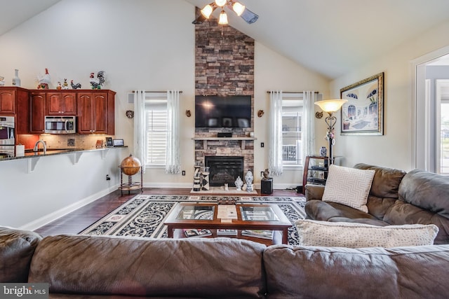 living room with dark wood-type flooring, a stone fireplace, high vaulted ceiling, sink, and ceiling fan