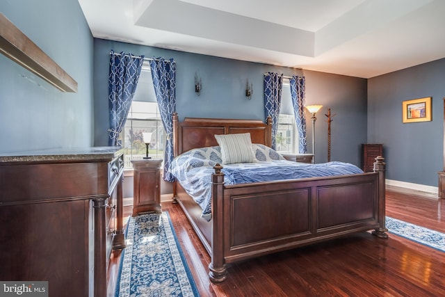 bedroom featuring dark wood-type flooring, a raised ceiling, and multiple windows