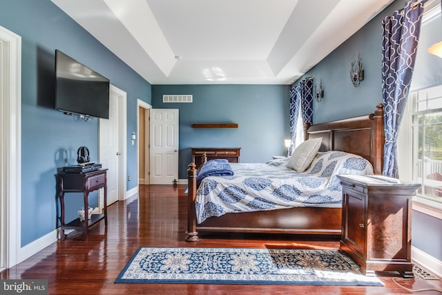 bedroom with dark hardwood / wood-style floors and a raised ceiling