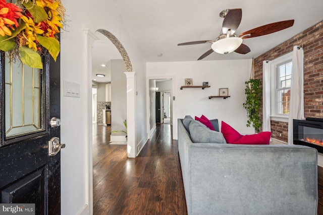 living room featuring ceiling fan, dark hardwood / wood-style floors, brick wall, and ornate columns