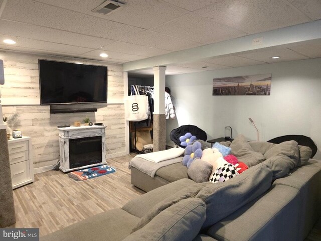 living room featuring wood walls, light hardwood / wood-style flooring, and a drop ceiling