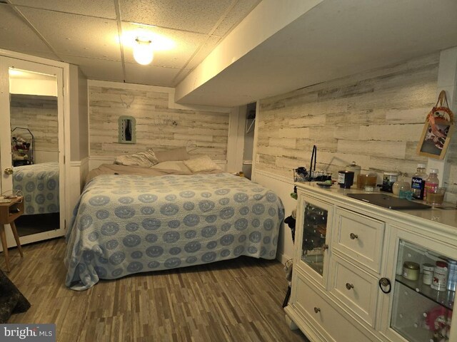 bedroom featuring a paneled ceiling, wood walls, dark hardwood / wood-style flooring, and sink