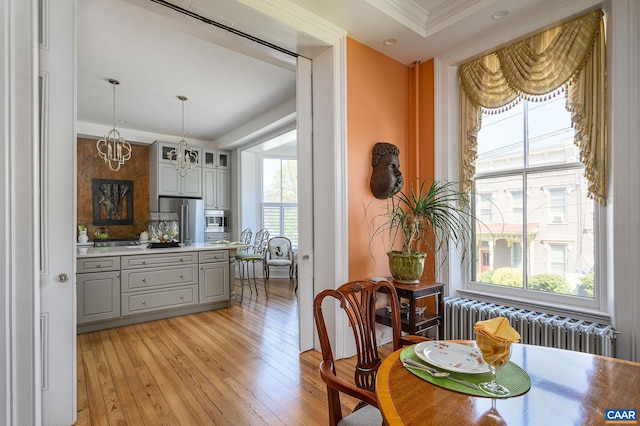 dining space with light hardwood / wood-style floors, a wealth of natural light, radiator, and a notable chandelier