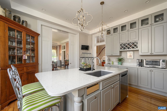 kitchen featuring stainless steel dishwasher, wood-type flooring, an inviting chandelier, sink, and a kitchen island with sink